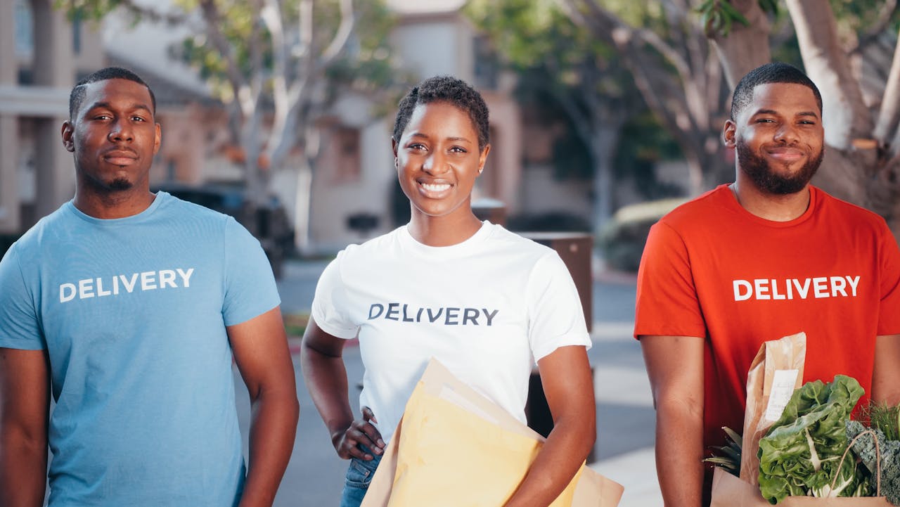 Three delivery team members holding packages with smiles outdoors, showcasing teamwork and service.