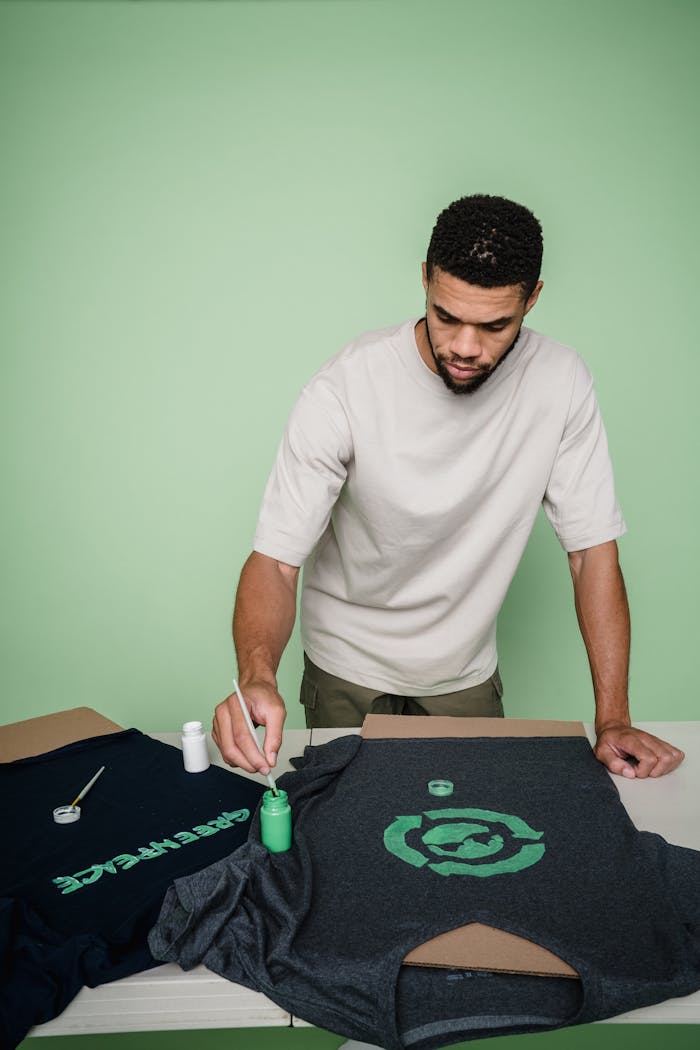 Man with beard painting custom designs on t-shirts in a studio setting.